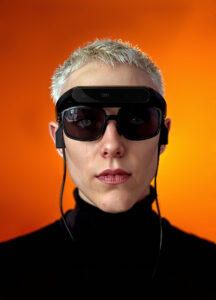 Persona joven usando las gafas inteligentes NIIRA de Eyesynth frente a fondo naranja, tecnología asistiva para personas con baja visión